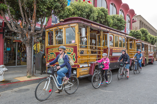 San Francisco, California, United States - August 14, 2016: Family of tourists with typical rental bike of San Francisco, in front of Cable Car Classic on wheels parked in Fisherman's Wharf area.