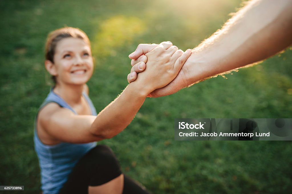 Man helping woman to stand up Close up shot of man helping woman to stand up. Focus on hands of couple exercising at park. A Helping Hand Stock Photo