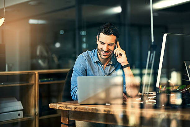 Inspiring productivity with a wealth of technology Shot of a young businessman talking on his phone and using a laptop during a late night at work business telephone mobile phone men stock pictures, royalty-free photos & images