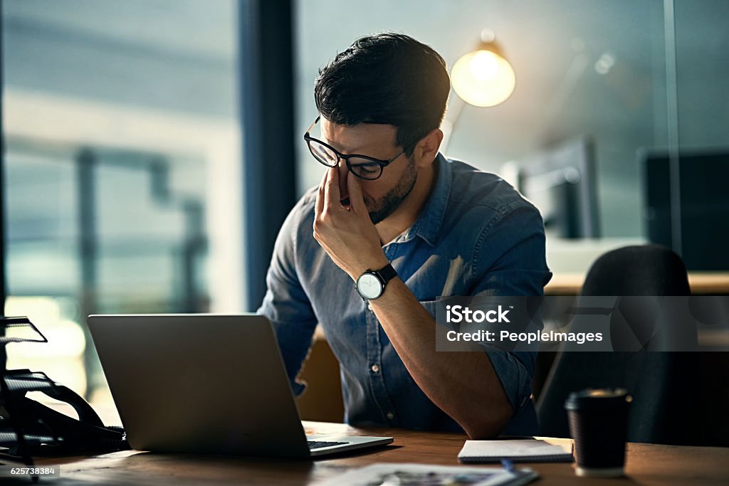 Burnout is killing his career Shot of a young businessman experiencing stress during a late night at work Emotional Stress Stock Photo