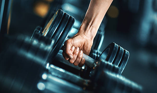 Heavy weight exercise. Closeup side view of unrecognizable woman grabbing a dumbbell from a dumbbell rack. Shallow focus, toned image. exercise machine photos stock pictures, royalty-free photos & images