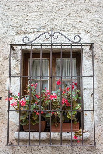 window and flowerbox. Window decorated. Vibrant Colorful Red flower in Metal Barred Window Box with Sandstone Surrounds 