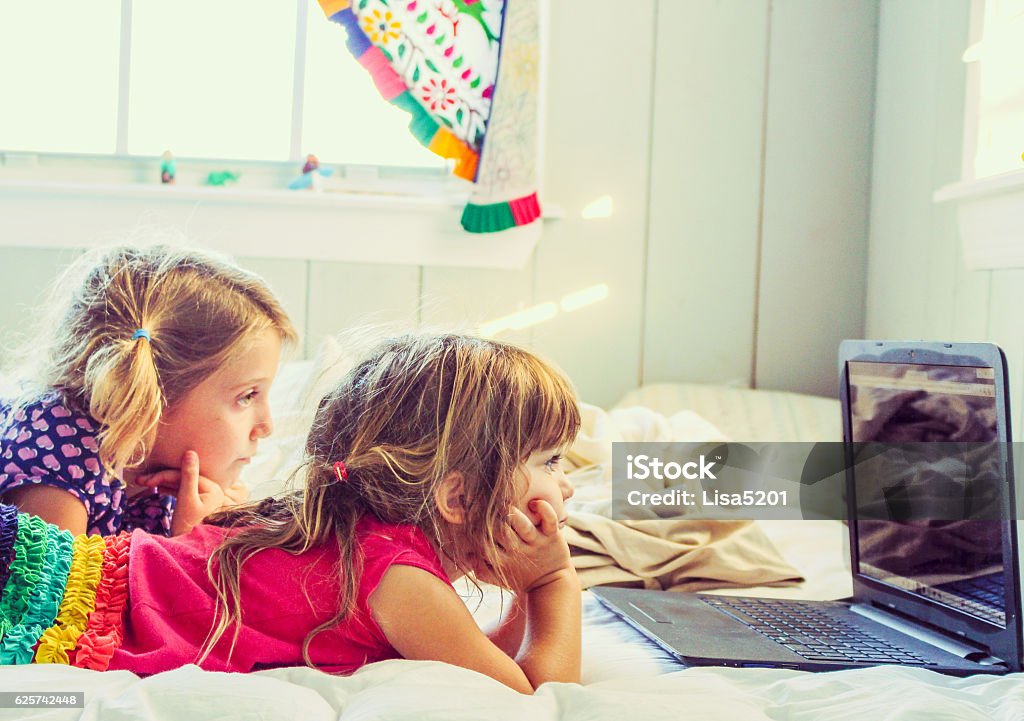 Watching Two little girls laying down and watching something on a laptop Screen Time - Concept Stock Photo