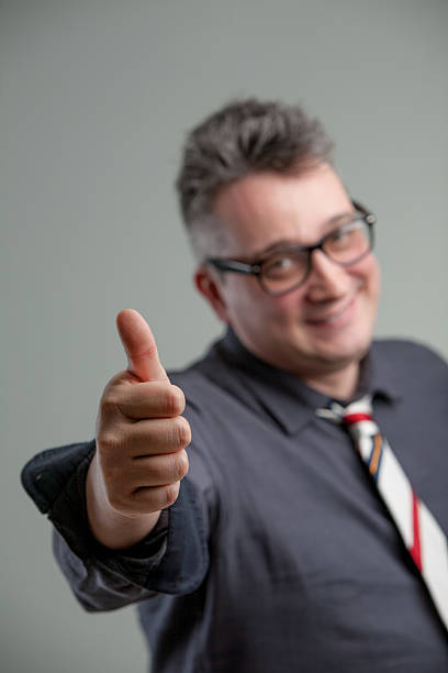 focus on thumb up with old man in background focus on thumb up of a middle-aged office worker agreeing with you accomodating stock pictures, royalty-free photos & images