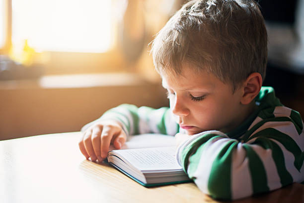 istock Little boy reading a book a the table 625743212