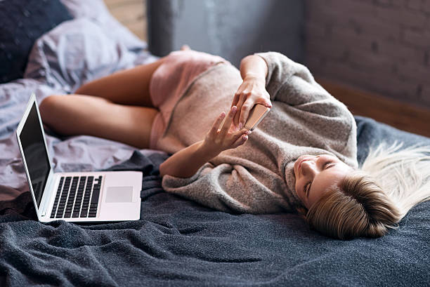 femme détendue utilisant un smartphone au lit - using computer bedroom one woman only cheerful photos et images de collection