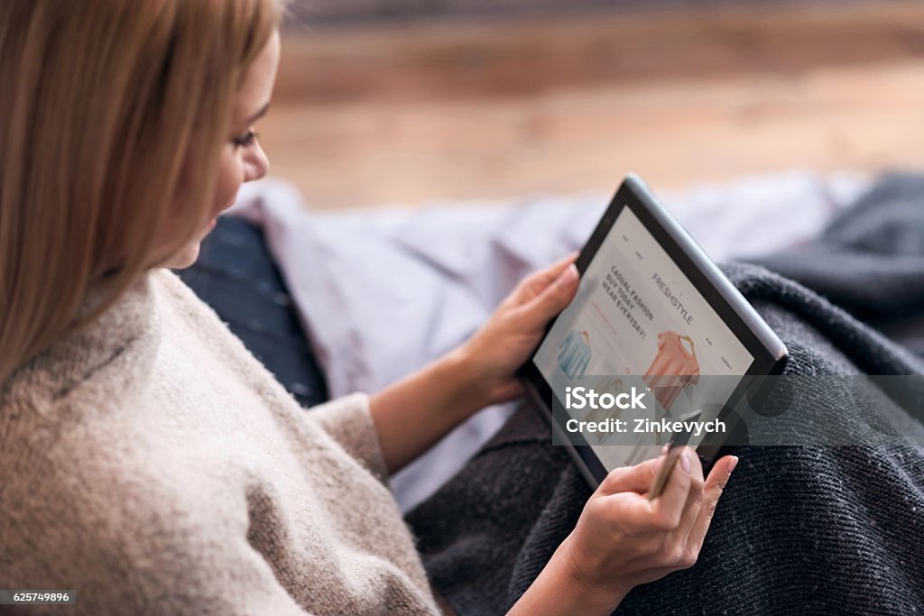 Joyful woman enjoying online shopping in bed Be trendy. Joyful young pretty woman enjoying online shopping and using tablet and credit card while sitting in bed. Internet Stock Photo