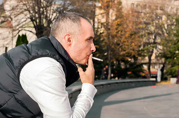 Photo of Handsome stylish young man smoking outside in urban setting