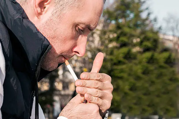 Photo of Handsome stylish young man smoking outside in urban setting