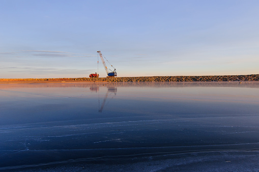 crane loading truck in harbor near from frozen river in clear weather on a background of blue sky