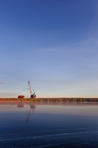 crane loading truck in harbor near from frozen river in clear weather on a background of blue sky