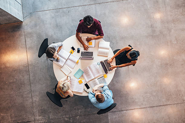 Young people studying together around a table Group of young students in cooperation with their academic assignment. Top view shot of young people studying together around a table. jacob ammentorp lund stock pictures, royalty-free photos & images
