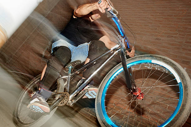 The guy's a cyclist in motion, riding on the rear wheel of the bike near the wall of the red brick building