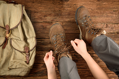 Young woman is putting on shoes for hiking on wooden floor