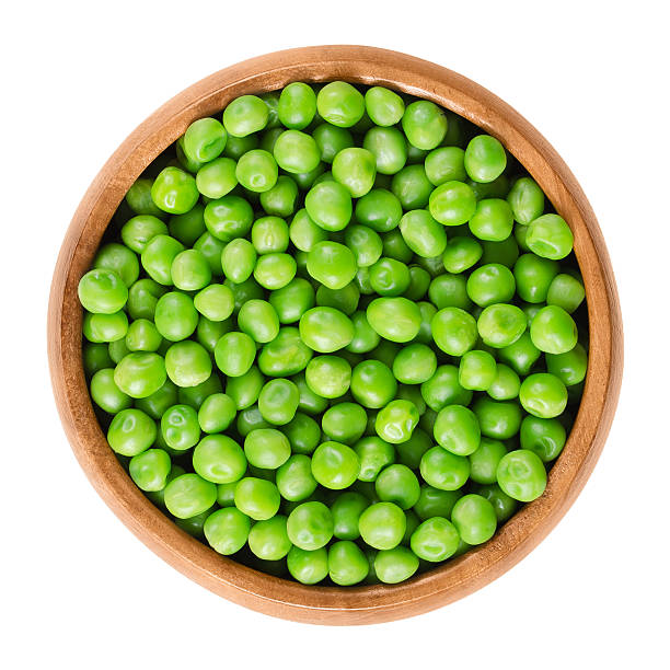 Raw peas in wooden bowl over white