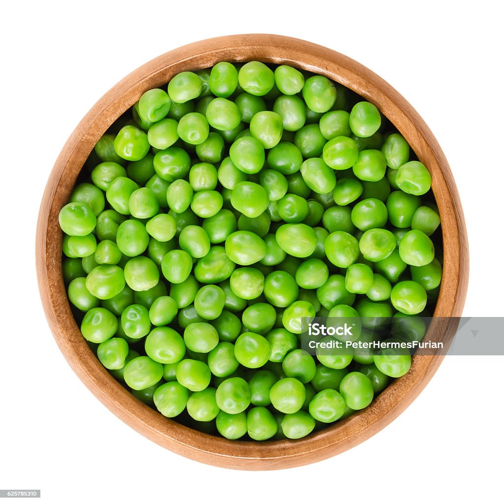 Raw peas in wooden bowl over white Raw peas in wooden bowl. Green small spherical seeds of the pod fruit Pisum sativum, an edible legume. Isolated macro food photo close up from above on white background. Green Pea Stock Photo