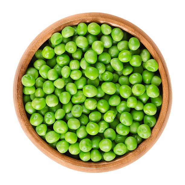 Raw peas in wooden bowl over white Raw peas in wooden bowl. Green small spherical seeds of the pod fruit Pisum sativum, an edible legume. Isolated macro food photo close up from above on white background. green pea stock pictures, royalty-free photos & images