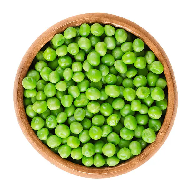 Raw peas in wooden bowl. Green small spherical seeds of the pod fruit Pisum sativum, an edible legume. Isolated macro food photo close up from above on white background.