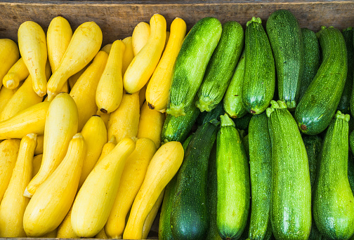 A wooden box full of green zucchini and bright yellow summer squash at a Cape Cod farmers market