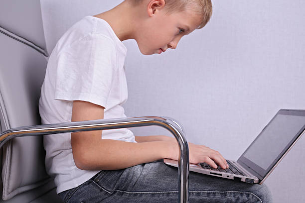 Children bad incorrect sitting posture. Boy using laptop computer stock photo
