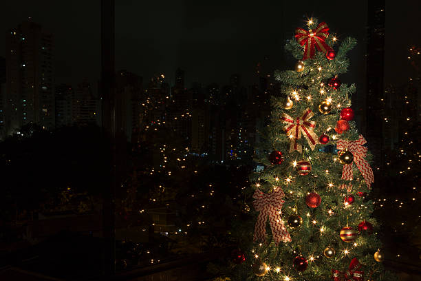Christmas tree with lights on, in front of a city landscape at night