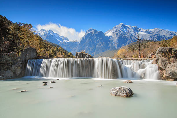 Waterfall and Jade Dragon Snow Mountain - Yunnan, China Waterfall on foreground and Jade Dragon Snow Mountain on background - Yunnan, China meili mountains photos stock pictures, royalty-free photos & images