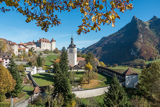 view of gruyeres in switzerland in fall looking from under fall leaves at gruyeres village, chateau and church with mountains and blue sky in the background. fribourg city switzerland stock pictures, royalty-free photos & images