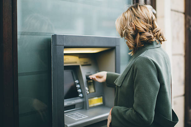 jeune femme à l'aide d'un distributeur automatique de billets - distributeur automatique photos et images de collection
