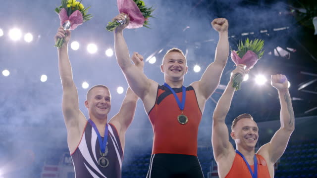 Enthusiastic male gymnasts cheering celebrating victory on medal podium