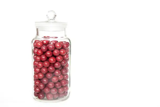 Vintage sweet shop jar full of retro aniseed ball sweets. Jar is isolated against a white background providing copyspace.