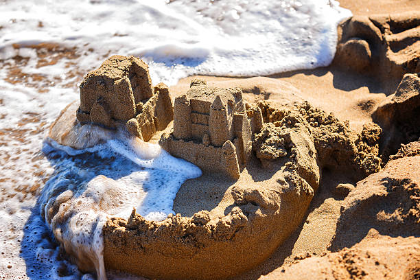 les vagues emportent les châteaux de sable sur la plage de la mer - sandcastle photos et images de collection