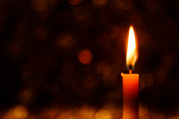A candle is lit and is sitting on a metal holder. The candle is yellow and orange, and the holder is silver. The image has a warm and cozy feeling, as if it were lit in a dimly lit room