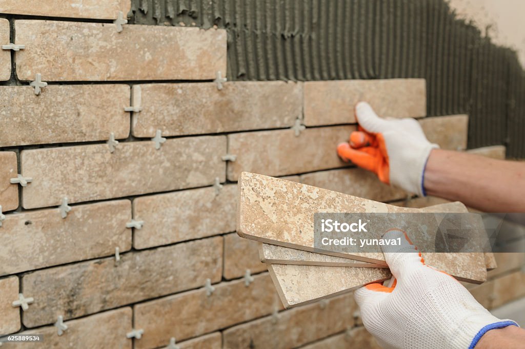 Installing the tiles on the wall. Installing the tiles on the wall. A worker putting tiles in the form of brick. Animal Body Part Stock Photo