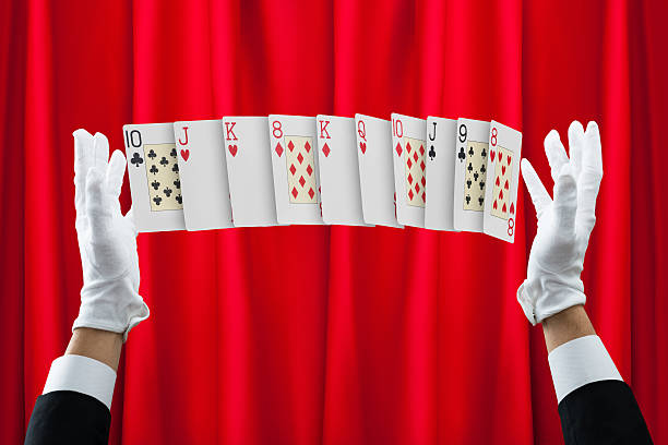 Cropped hands of magician performing trick with cards against red curtain