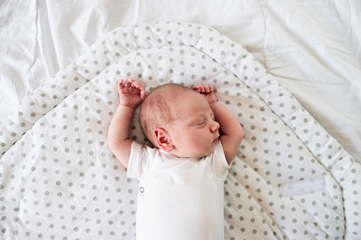 Cute little newborn baby boy lying on bed, sleeping, hands up. Close up.