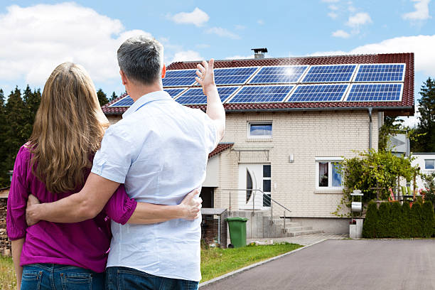 Couple Standing In Front Of Their House Rear View Of Couple Standing In Front Of Their House solar power station solar panel house solar energy stock pictures, royalty-free photos & images
