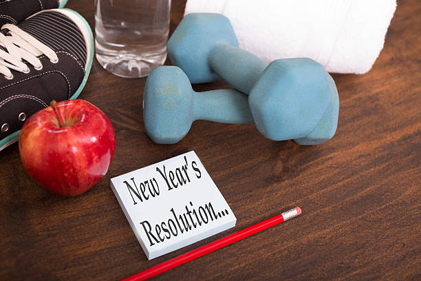 New Year's Resolution to get healthy. New Year's Resolution to get healthy in January of the coming year. Image features: dumbbells, sports shoes, water bottle, red apple, towel, pencil on wooden table. Adhesive note reading "New Year's Resolution..." in foreground. Fitness, New Year's concept. 2019 new year resolution stock pictures, royalty-free photos & images