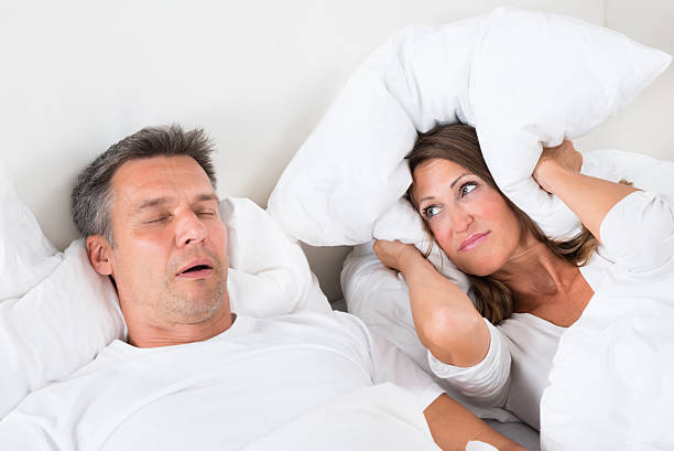 Angry Woman Trying To Sleep With Snoring Man Woman Covering Her Ears With Pillow While Man Snoring sleep apnea photos stock pictures, royalty-free photos & images