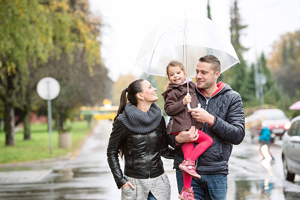 rodzina z córką pod parasolami spacer w deszczowy dzień. - puddle street water women zdjęcia i obrazy z banku zdjęć