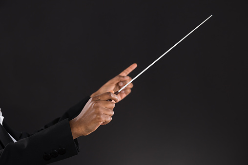 Close-up Of Female Orchestra Conductor Holding Baton Over Black Background