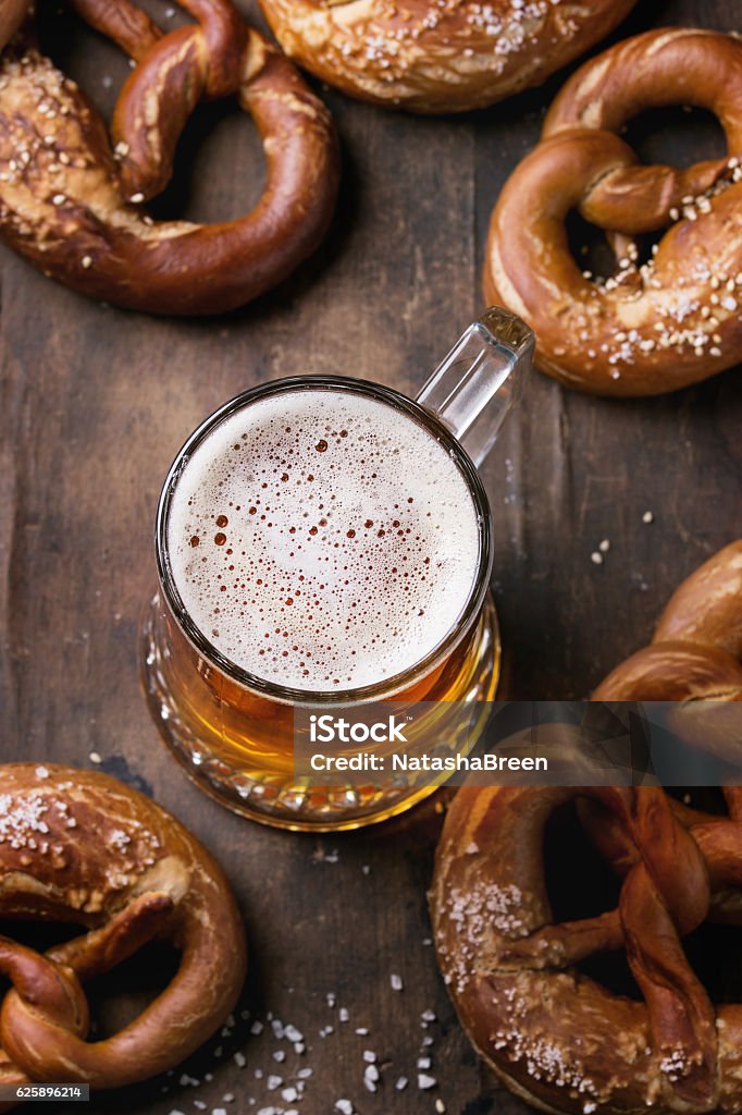 Lager beer with pretzels Glass of lager beer with traditional salted pretzels over old dark wooden background. Top view with space for text. Beer Fest theme. Selective focus on beer foam. Baked Pastry Item Stock Photo
