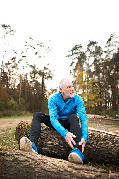 старший бегун сидит на деревянных бревнах, человек отдыхает, растягивается. - senior adult shoelace human leg leg стоковые фото и изображения