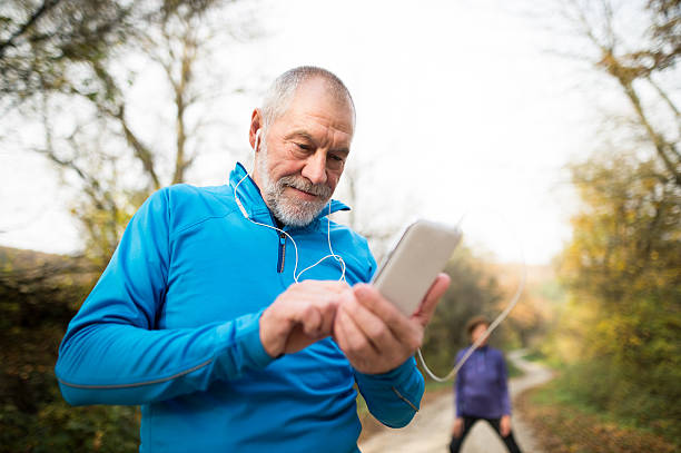 coureurs seniors dans la nature, étirements. homme avec smartphone avec e - senior couple audio photos et images de collection