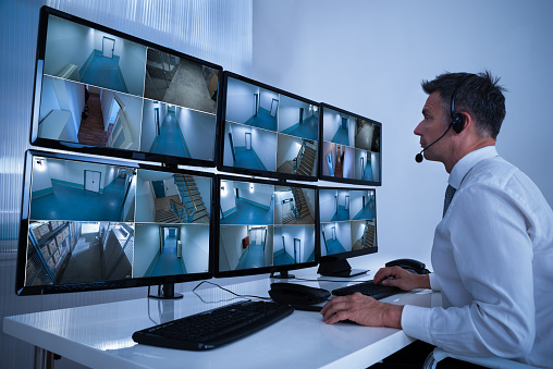 Rear view of security system operator looking at CCTV footage at desk in office