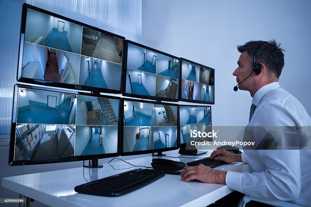 Security System Operator Looking At CCTV Footage At Desk Rear view of security system operator looking at CCTV footage at desk in office Security Stock Photo