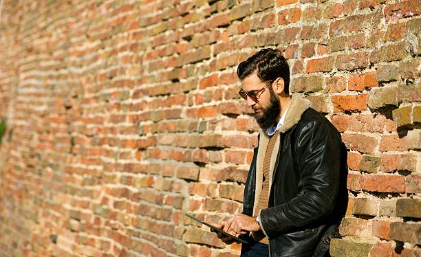 istock Handsome man with digital tablet leaning on brick wall. 625905296