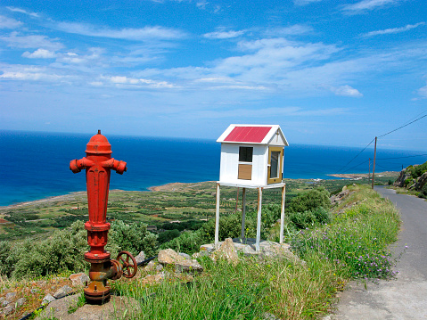 Red fire hydrant near road leading to the sea. Top view from road on the sea and panorama of coastline of Crete island.