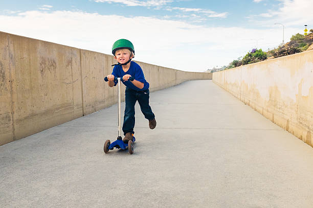 Little Boy Riding His Scooter Down A Bike Path