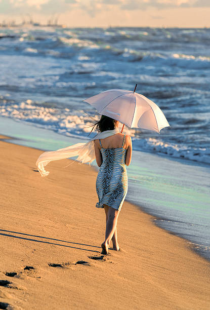 istock Rear view at woman with white umbrella walking on beach 625915662