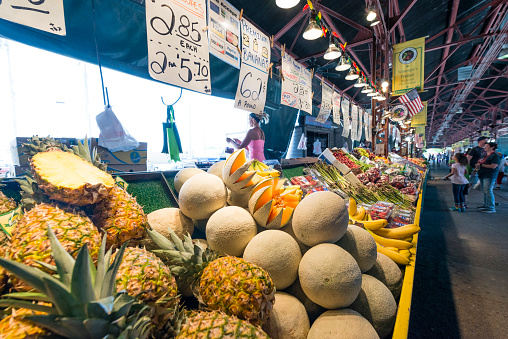 St. Louis, United States - May 6, 2016: At the Soulard farmers market rows full of a variety of produce, including pineapple, cantaloupe and bananas, are set out on display along a walking aisle for shoppers.